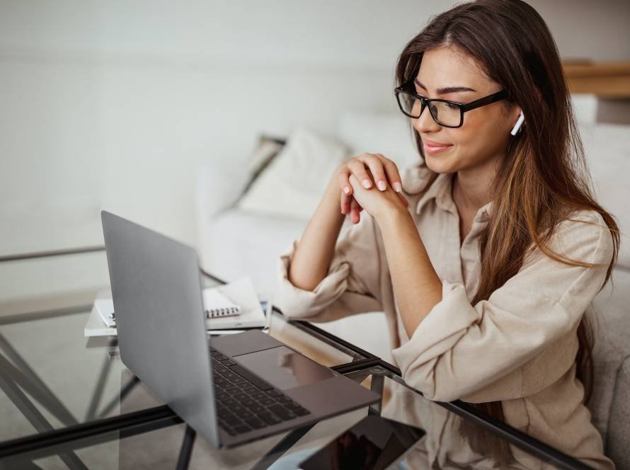 Smiling millennial mixed race woman in wireless headphones and glasses has video call on laptop