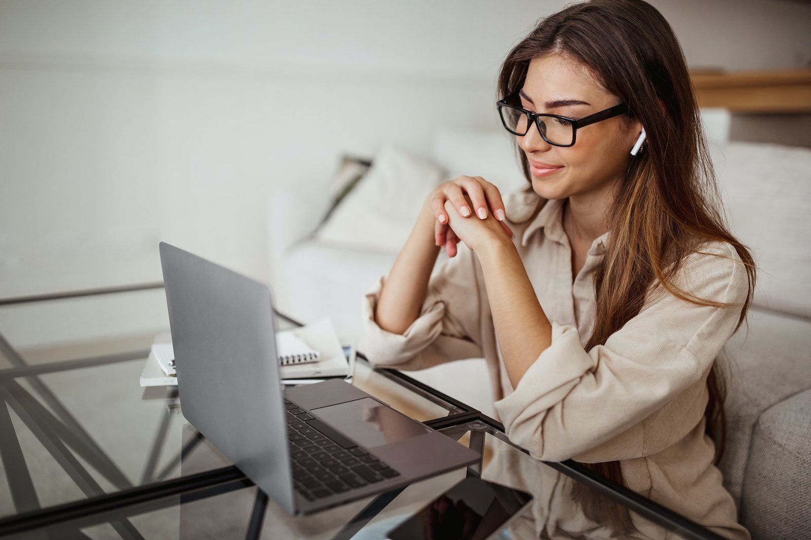 Smiling millennial mixed race woman in wireless headphones and glasses has video call on laptop